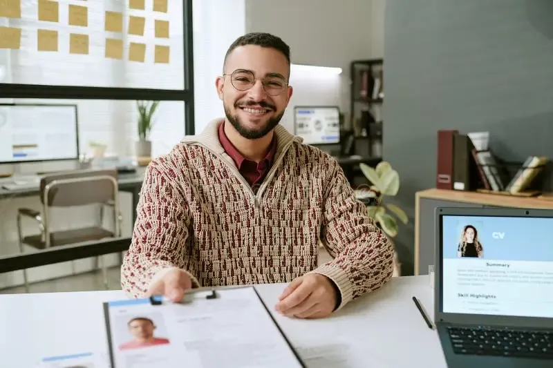Hombre sonriendo mientras sostiene y revisa su currículum impreso con orgullo